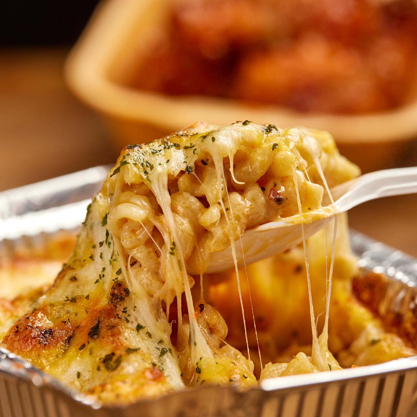 A forkful of mac and cheese stretching out of the foil tray