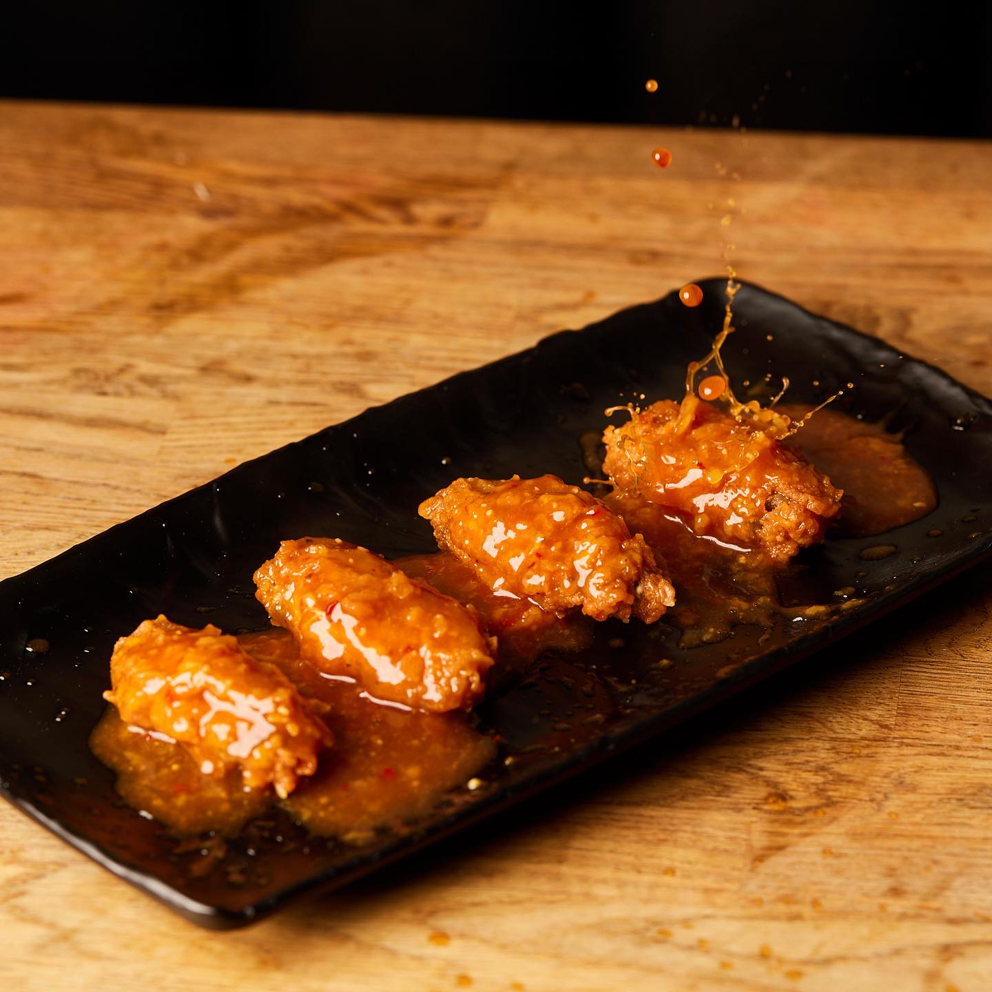 Glazed fried chicken on a black slate, sauce splashing